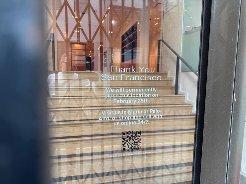 A closing notice on a San Francisco storefront window thanking the city and announcing the location will permanently close on February 26th, with a QR code and an empty staircase behind the glass.